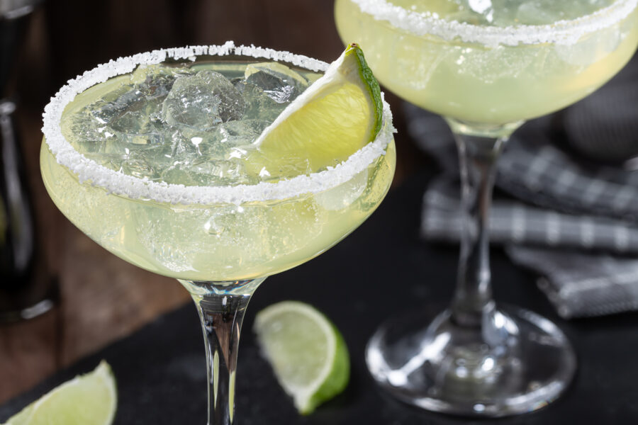 Margarita cocktail with ice, lime and salt rim on a black slate board