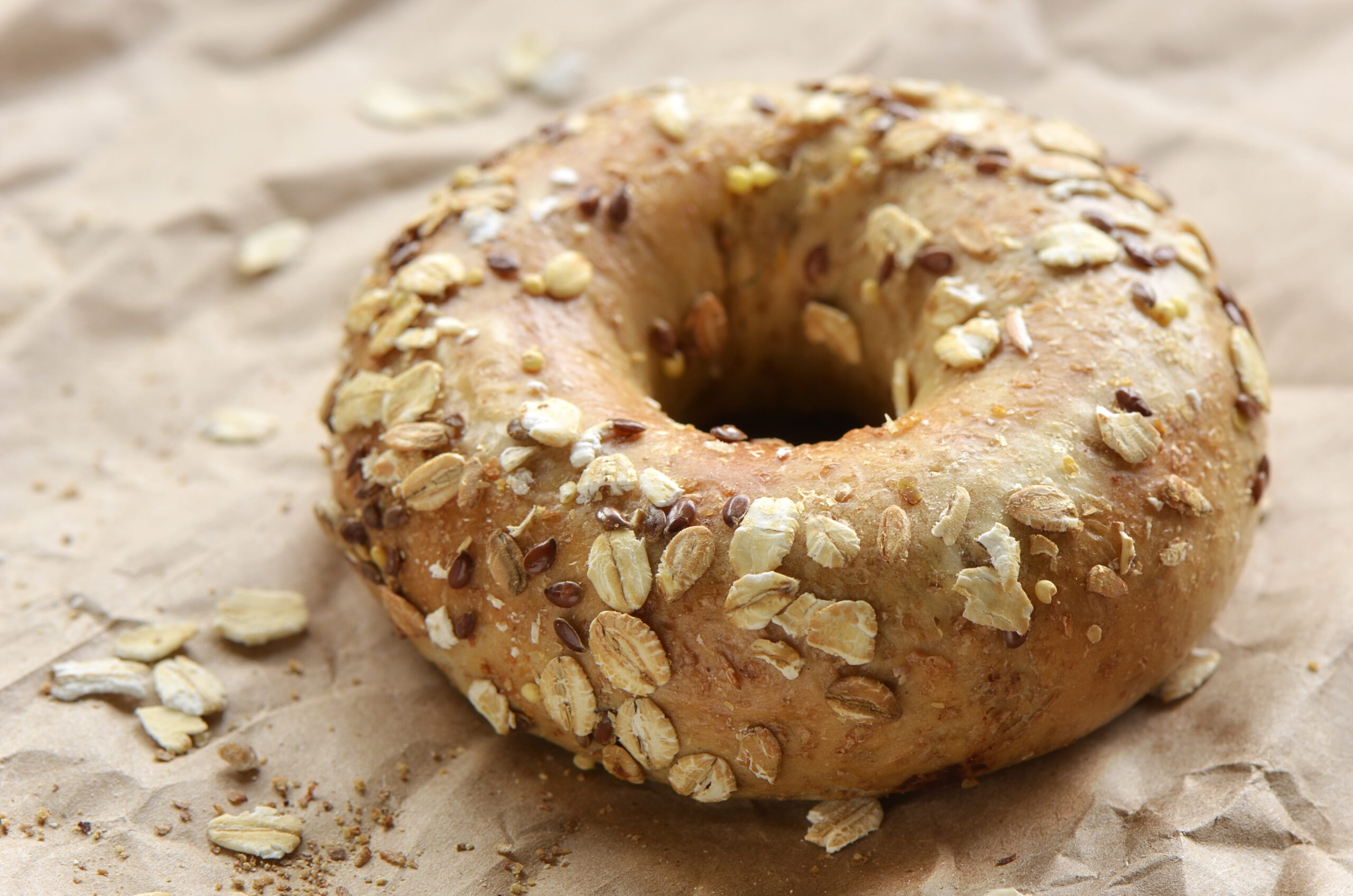 Multigrain bagel covered in oats and seeds on crinkled brown paper
