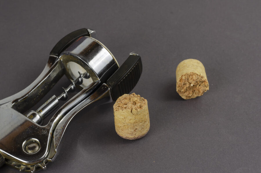 Old corkscrew and broken cork on a gray background. The corkscrew lies next to a broken wine cork. Selective focus