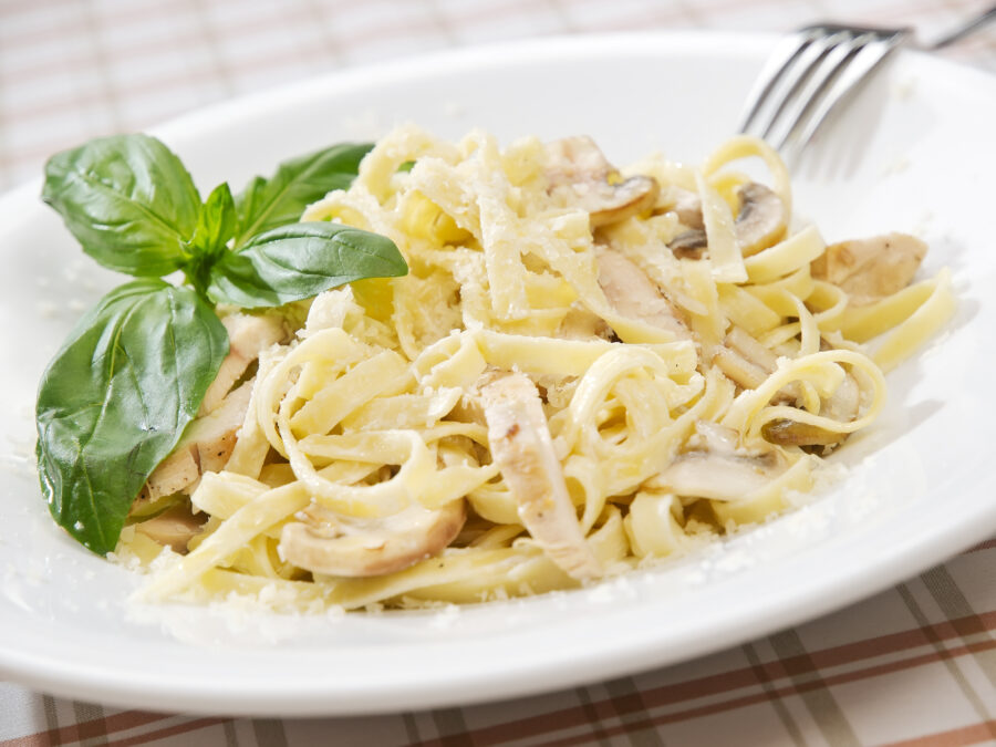 Pasta fettuccine alfredo with chicken, parmesan and parsley on blue wood background close up.