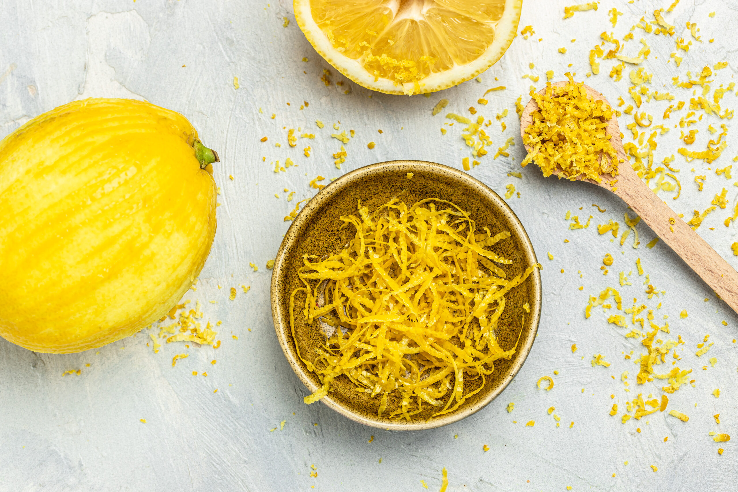 Peeling lemon rind to add zest to Mediterranean recipes. Grater peel and lemon zest on light background. top view,