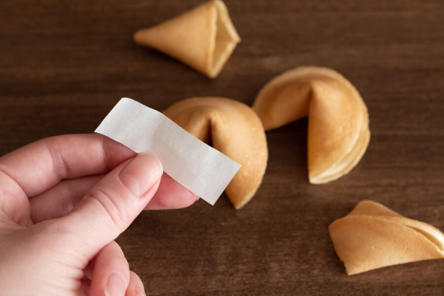 Person holds in hand blank paper slip from fortune cookie against few cookies laying on table surface background