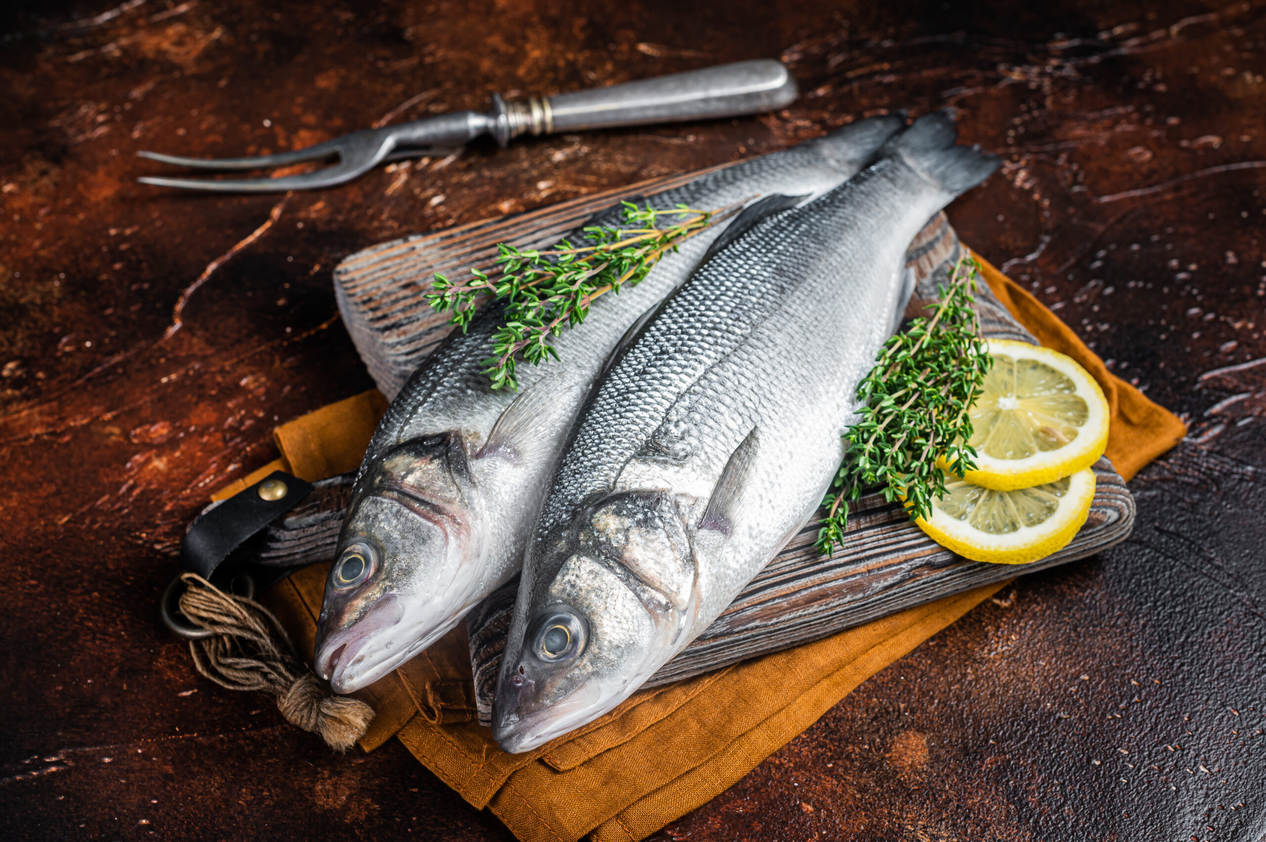 Raw Sea Bass, Branzino fish with thyme and lemon. Dark background. Top view.