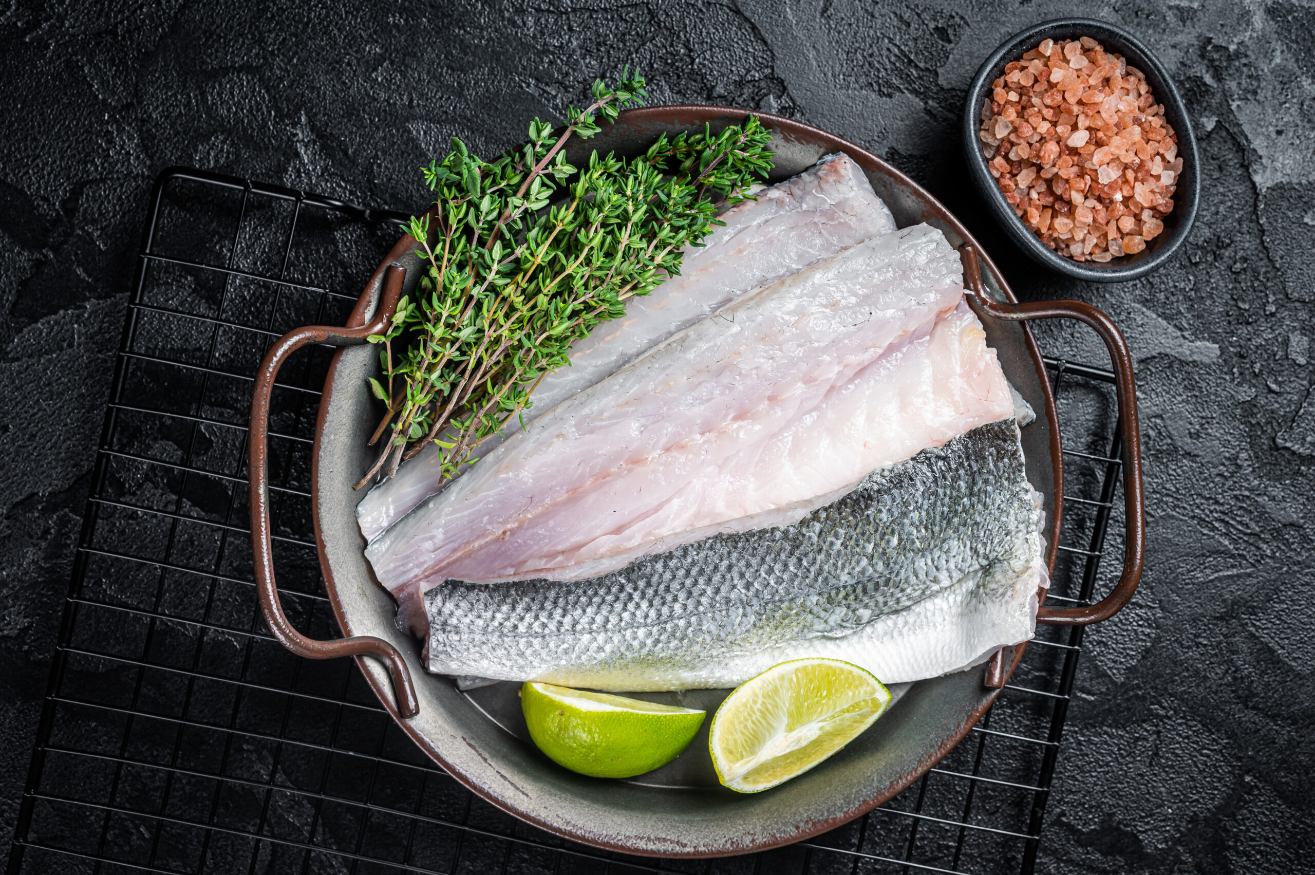 Raw Sea Bass fillet, Labrax fish with herbs and lime. Black background. Top view.