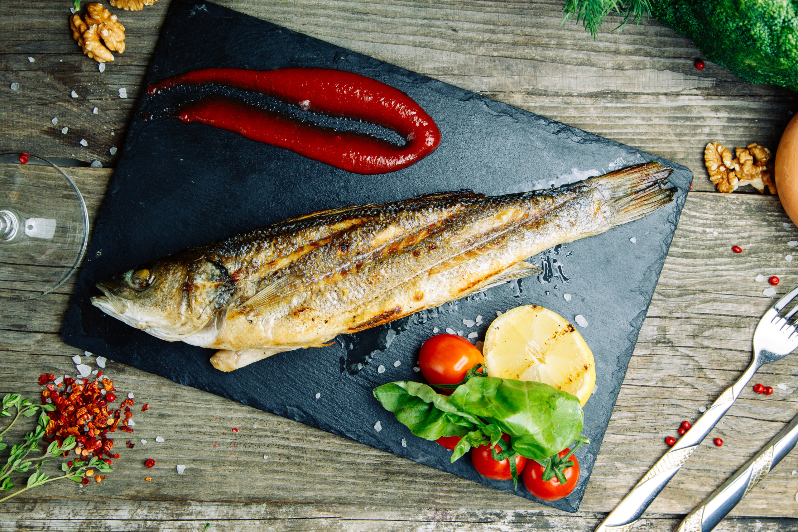 Restaurant dish with vegetable decor on a wooden background. Sea fish fried on a plate with sauce.