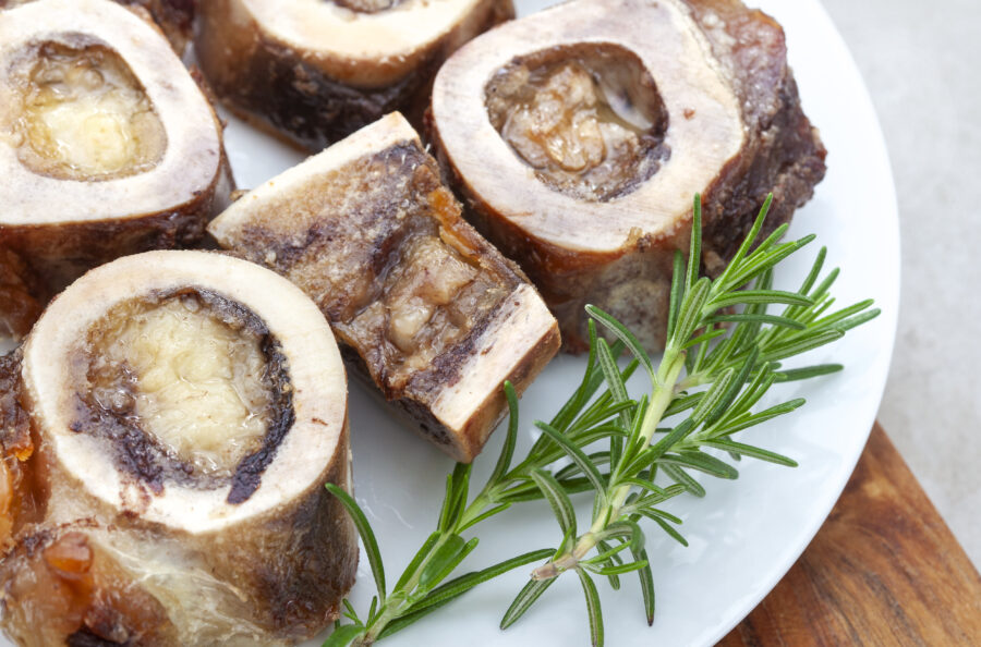 Roasted marrow bones on a white plate with rosemary garnish