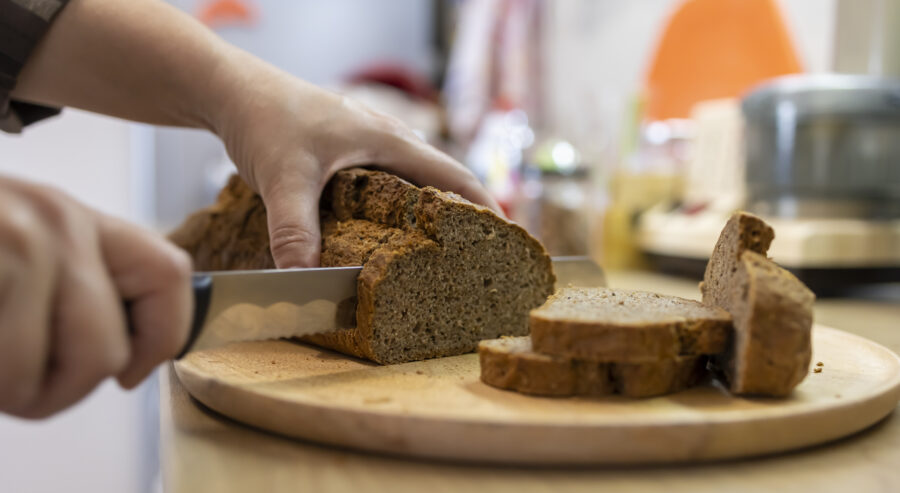 Shot of an unrecognizable woman cutting a loaf of brown bread