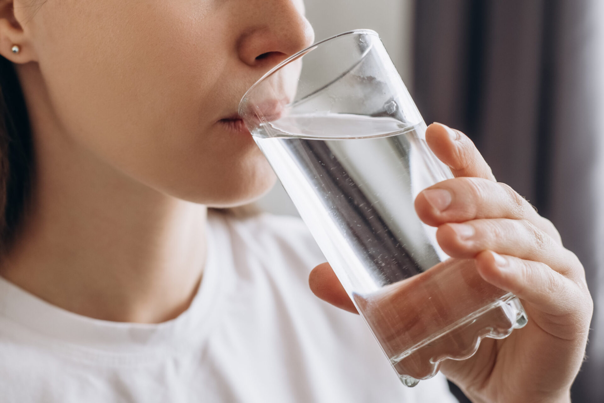 Side view close up of young female drinking pure still water in morning.