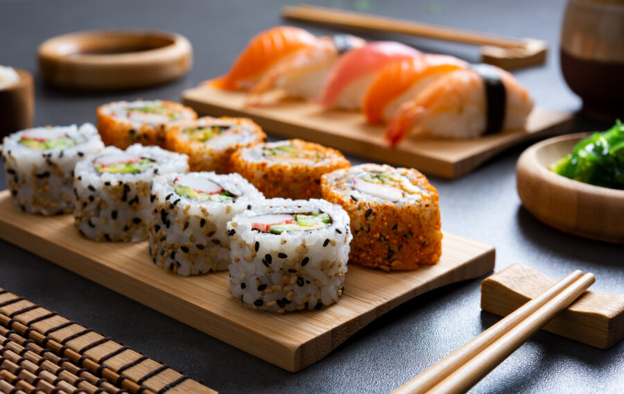 Sushi set uramaki and spicy sushi rolls served on bamboo tray. Various kinds of sushi pieces served on black slate with wooden chopstick.