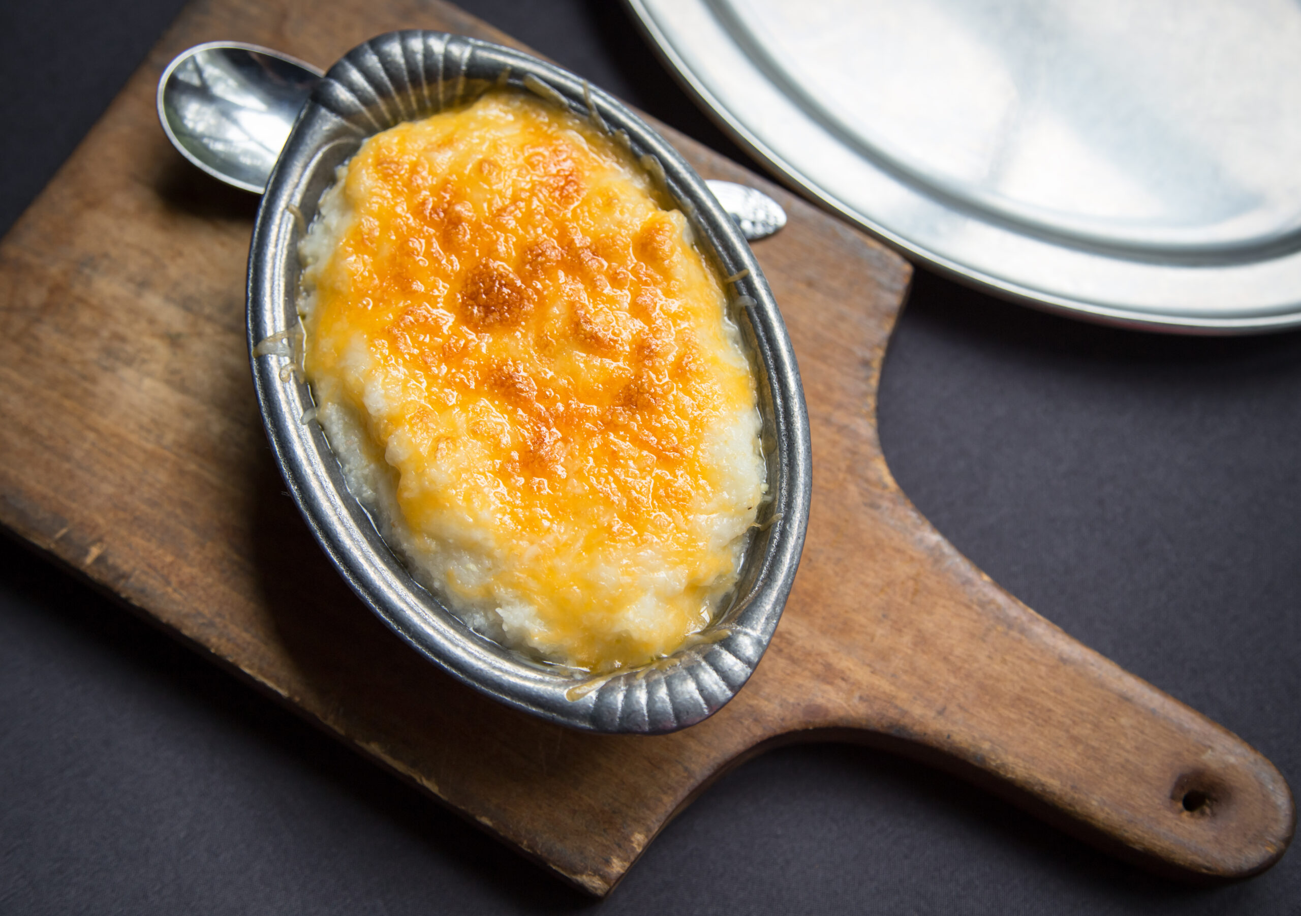 Top view of a small silver dish filled with grits with cheddar cheese topping.