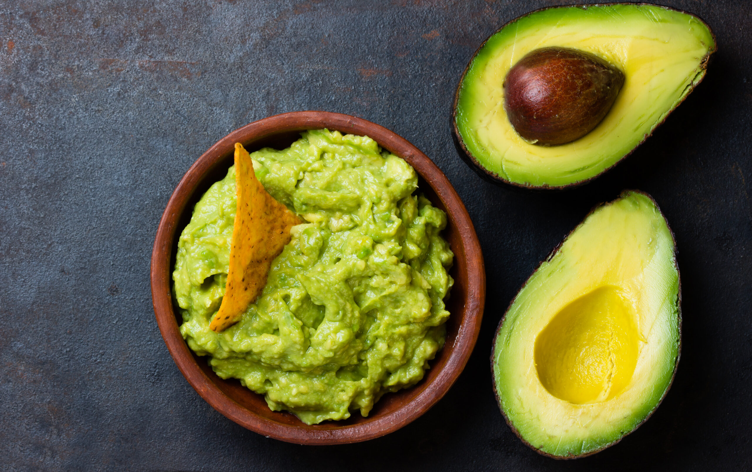 Traditional latinamerican mexican sauce guacamole in clay bowl and avocado sandwiches on dark background. Top view