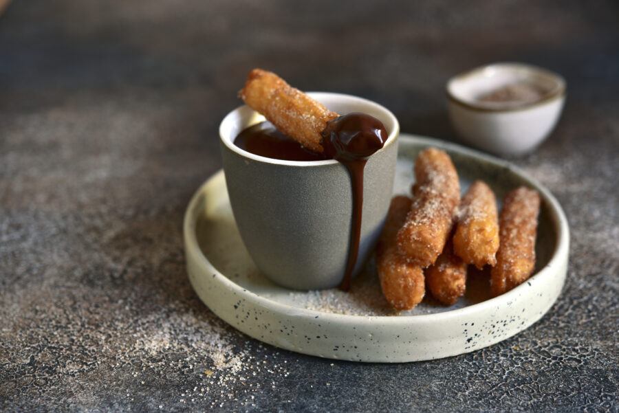 Traditional spanish dessert churros - fried choux pastry with chocolate sauce on a plate on a dark slate, stone or concrete background.