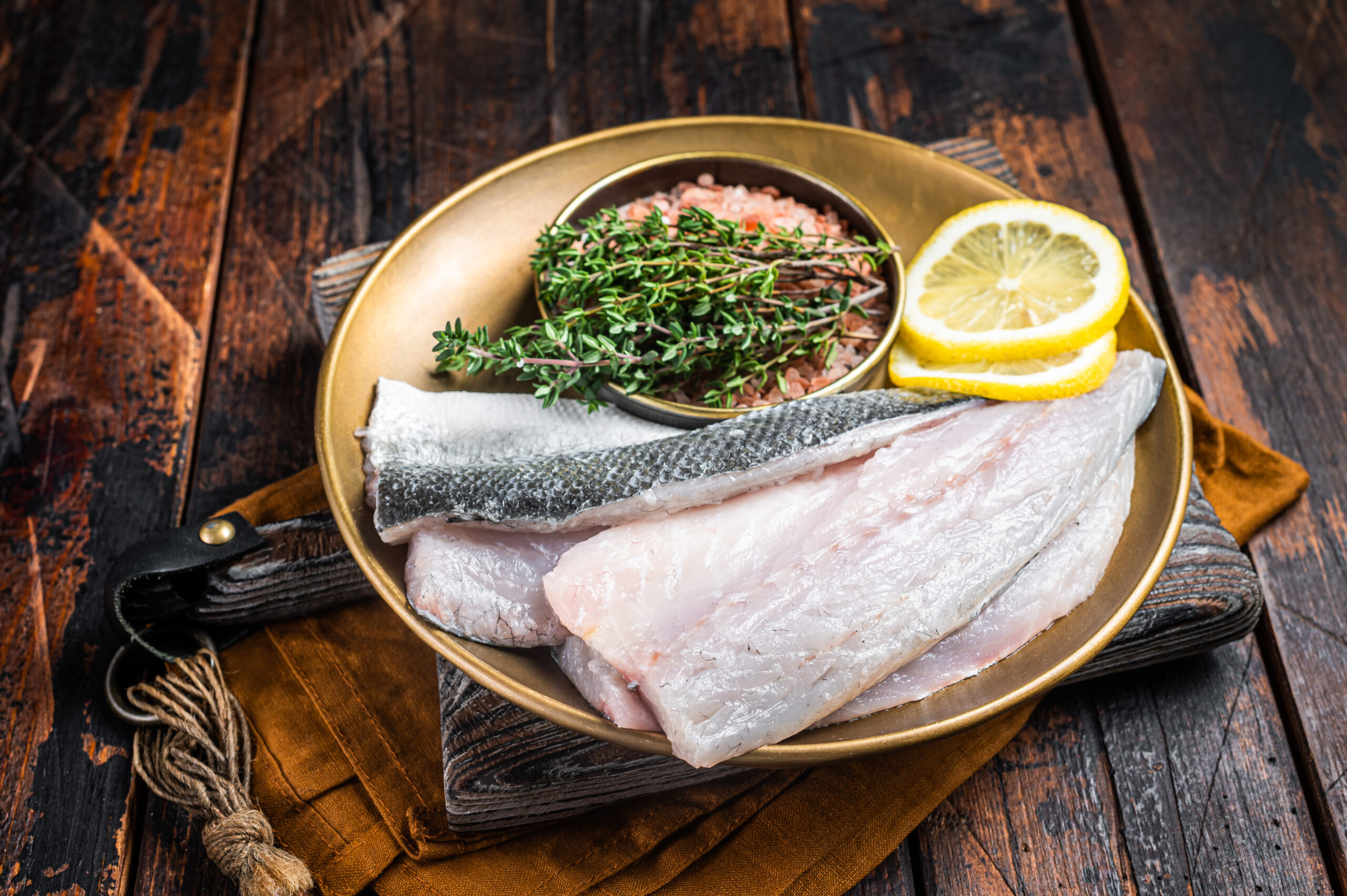 Uncooked Raw Sea Bass fillets, Seabass fish with thyme, pink salt and lemon. Dark background. Top view.