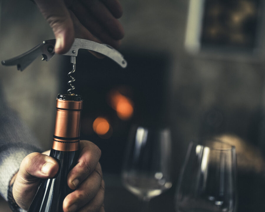 person opening wine bottle with corkscrew