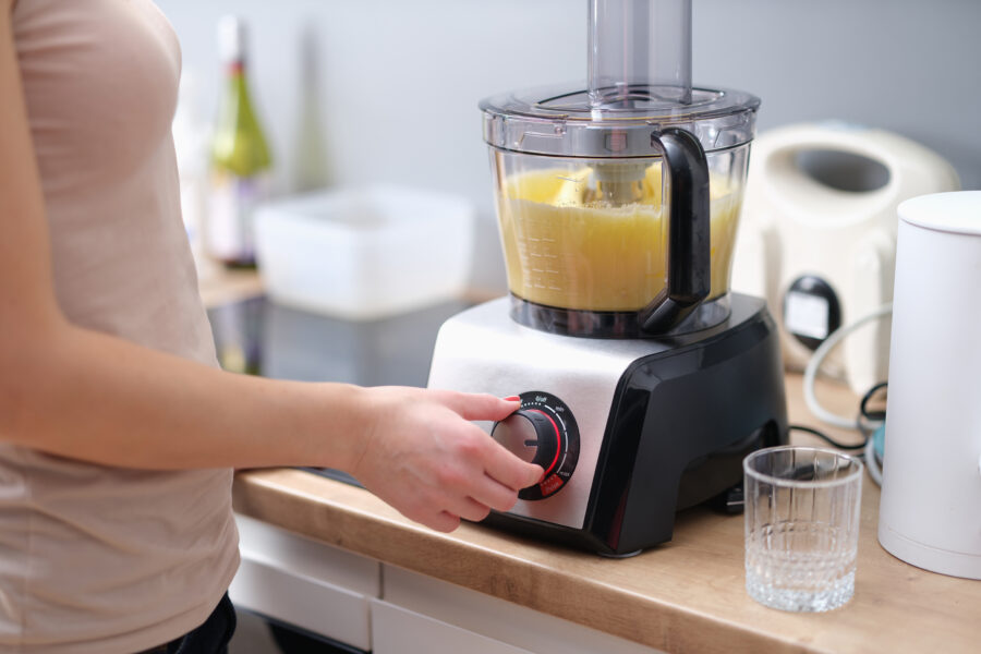 Woman cook turning on button of food processor for kneading dough closeup. 