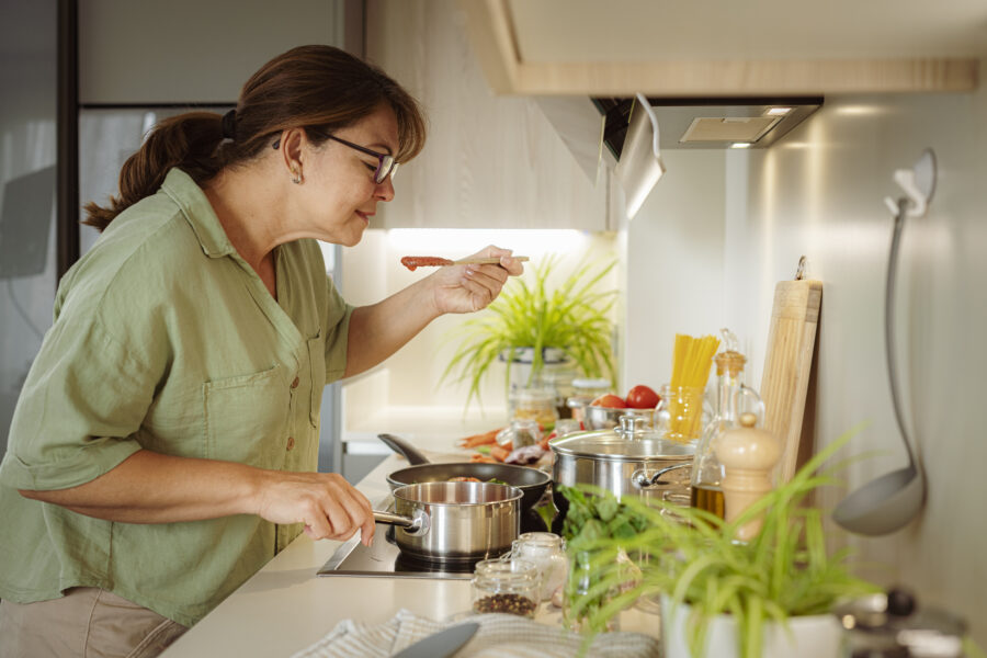 Woman cooking spaghetti and tasting tomato sauce