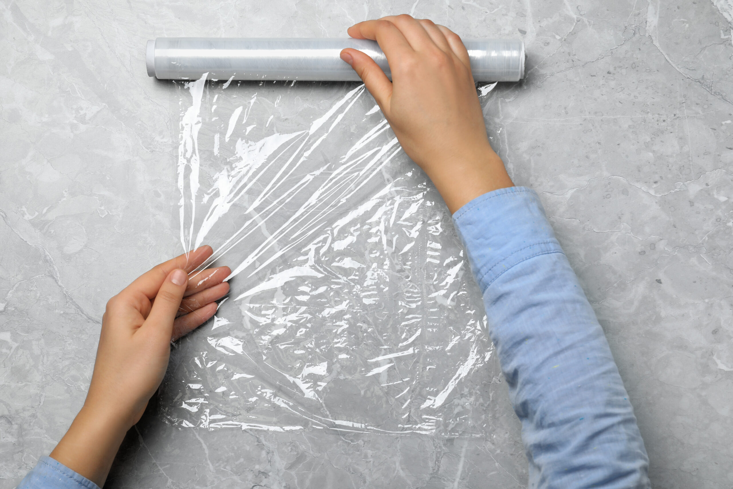 Woman with roll of stretch wrap at light grey table, top view