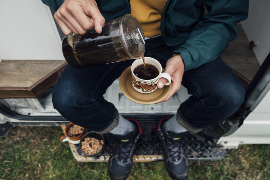 A directly above shot of a young man sitting on the side of his motor home pouring a cup of coffee.