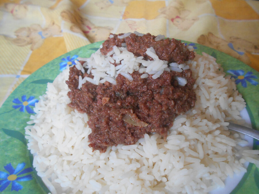 A green floral plate full of corned beef and rice sitting on the bed.