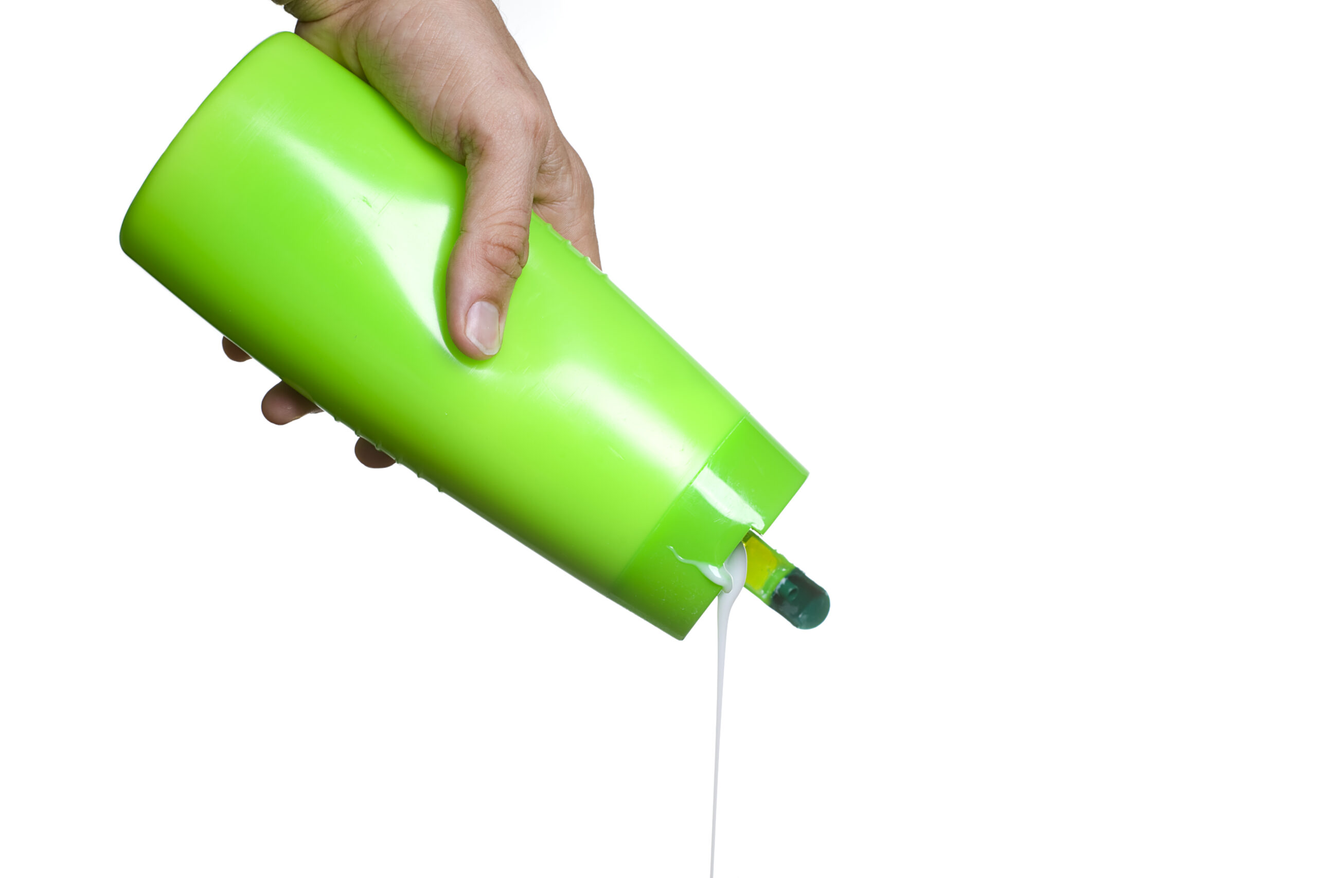 A hand holding a shampoo bottle pouring shampoo out.  White background.