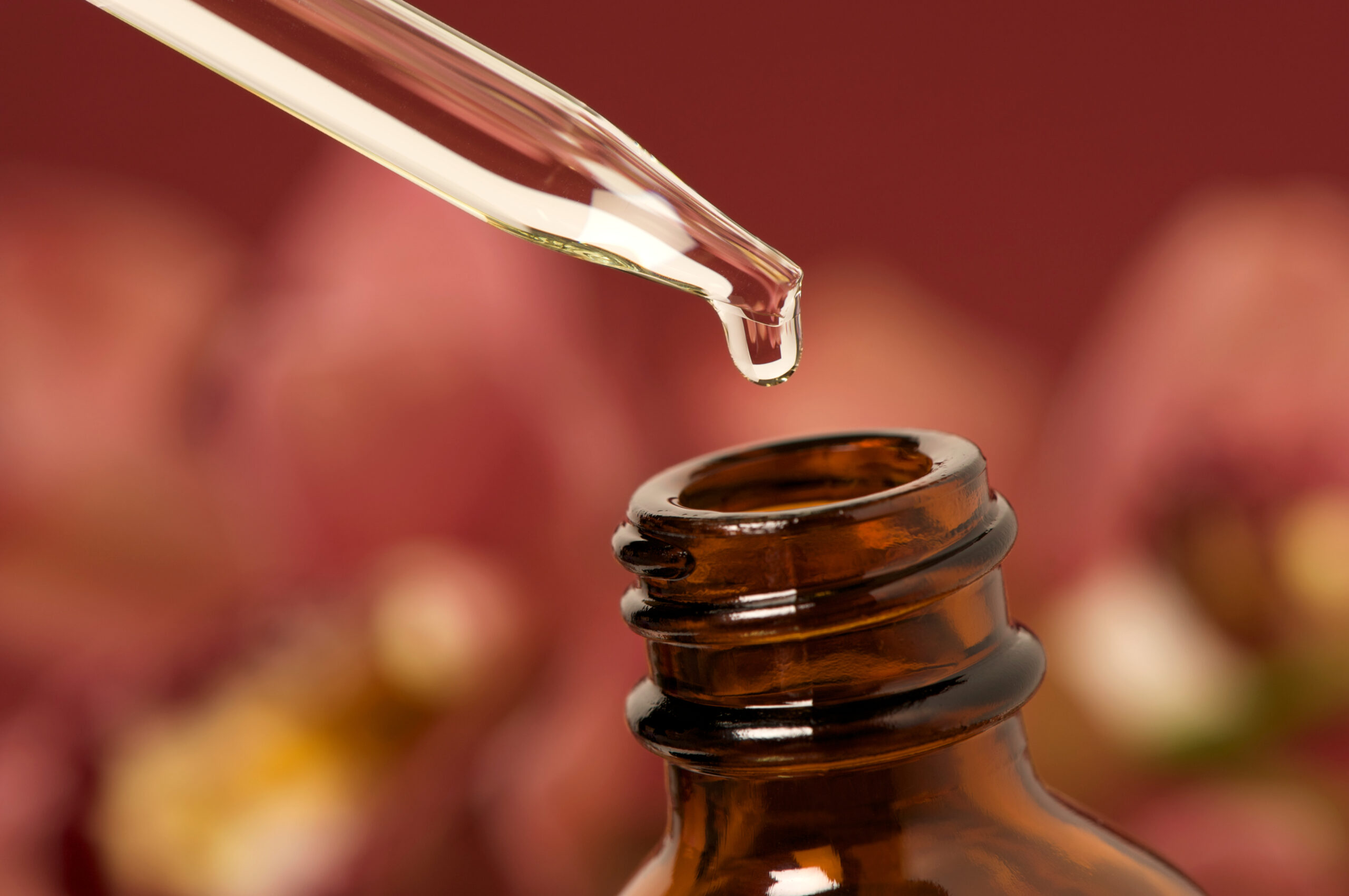 A pipette and bottle of essential oil with a soft abstract orchid background. Shallow depth of field.