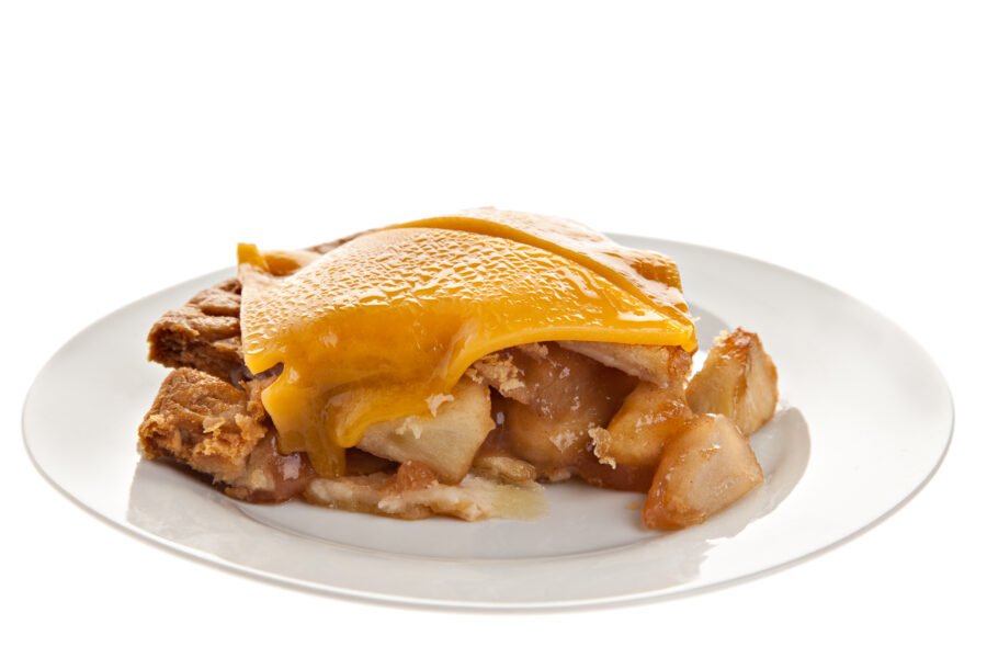 A side view of a delicious fresh homemade apple pie with a slice of melted cheddar cheese on top.