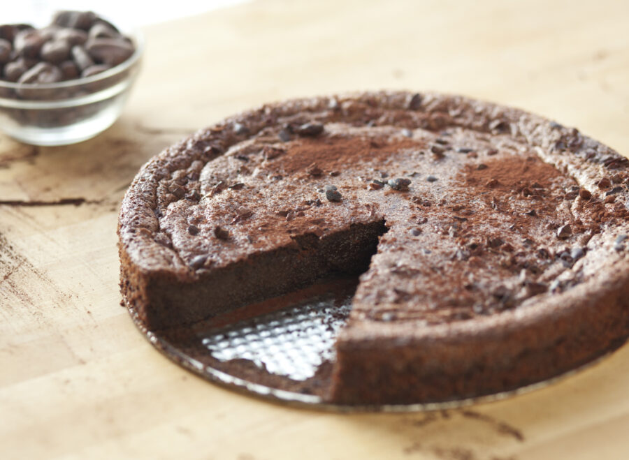 A whole chocolate cake dusted with cocoa and cocoa nibs with one slice missing.