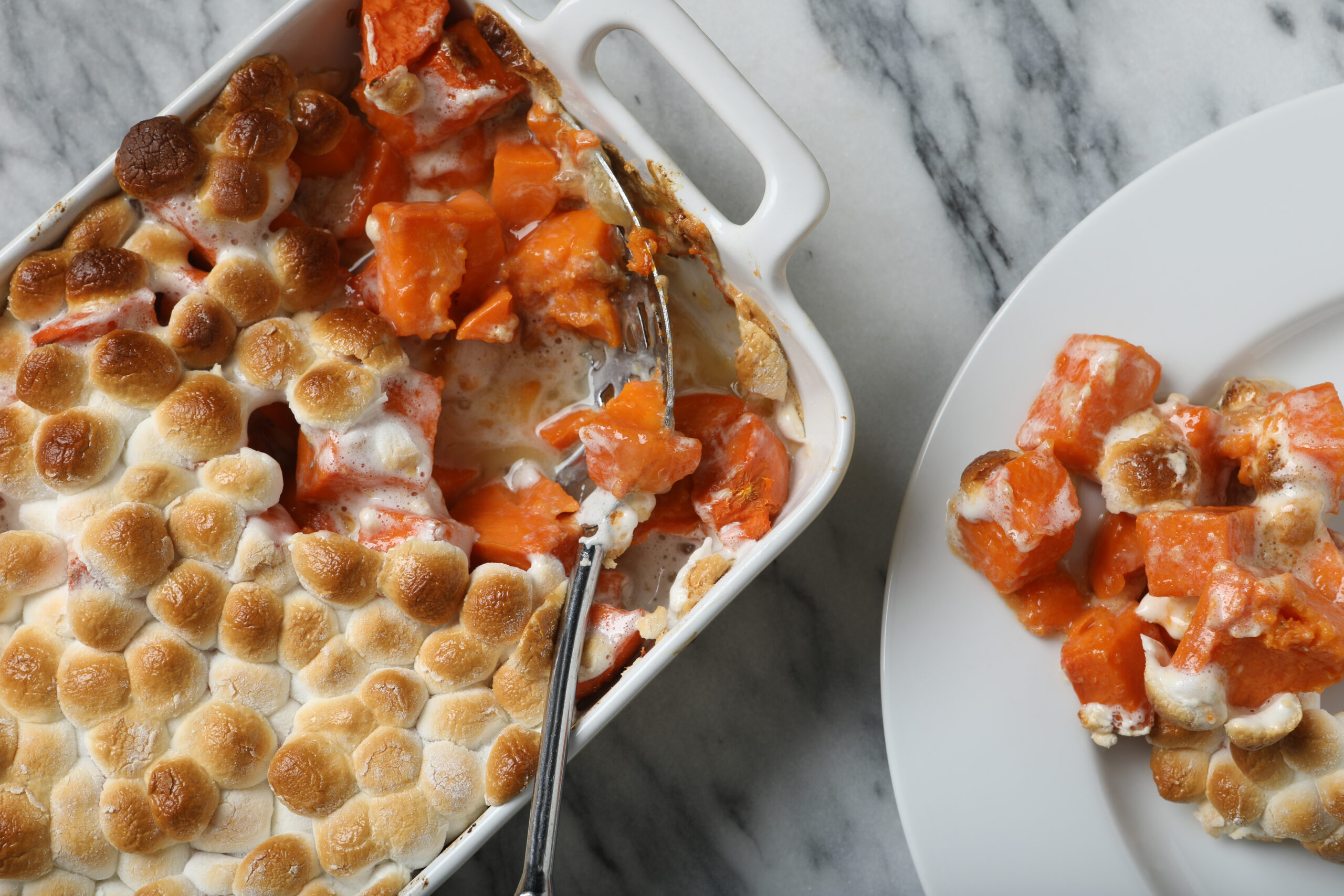 An overhead extreme close up horizontal photograph of  a Thanksgiving sweet potato casserole dish and a serving of the potatoes on a white plate.