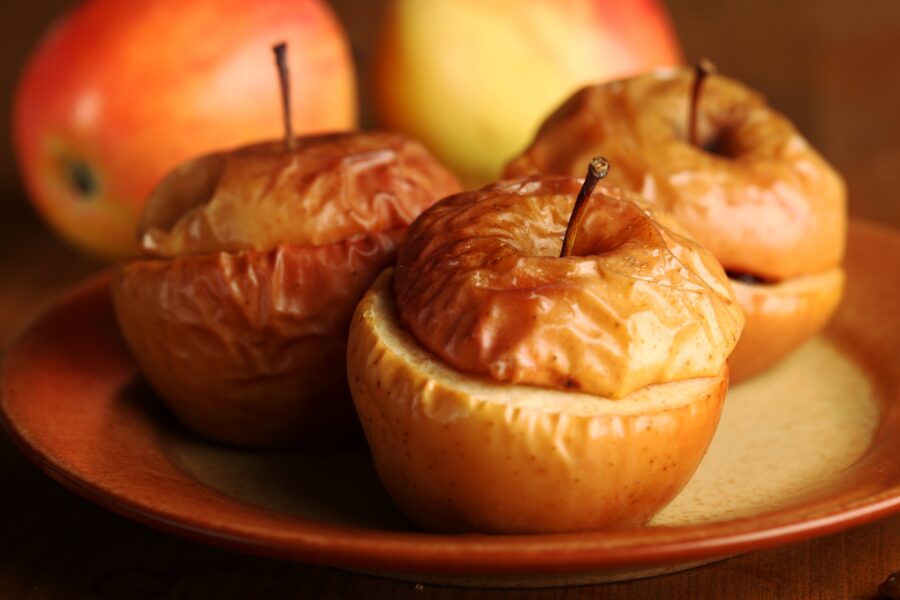 Baked stuffed apples on plate and fresh apples in the background. Selective focus, shallow DOF.