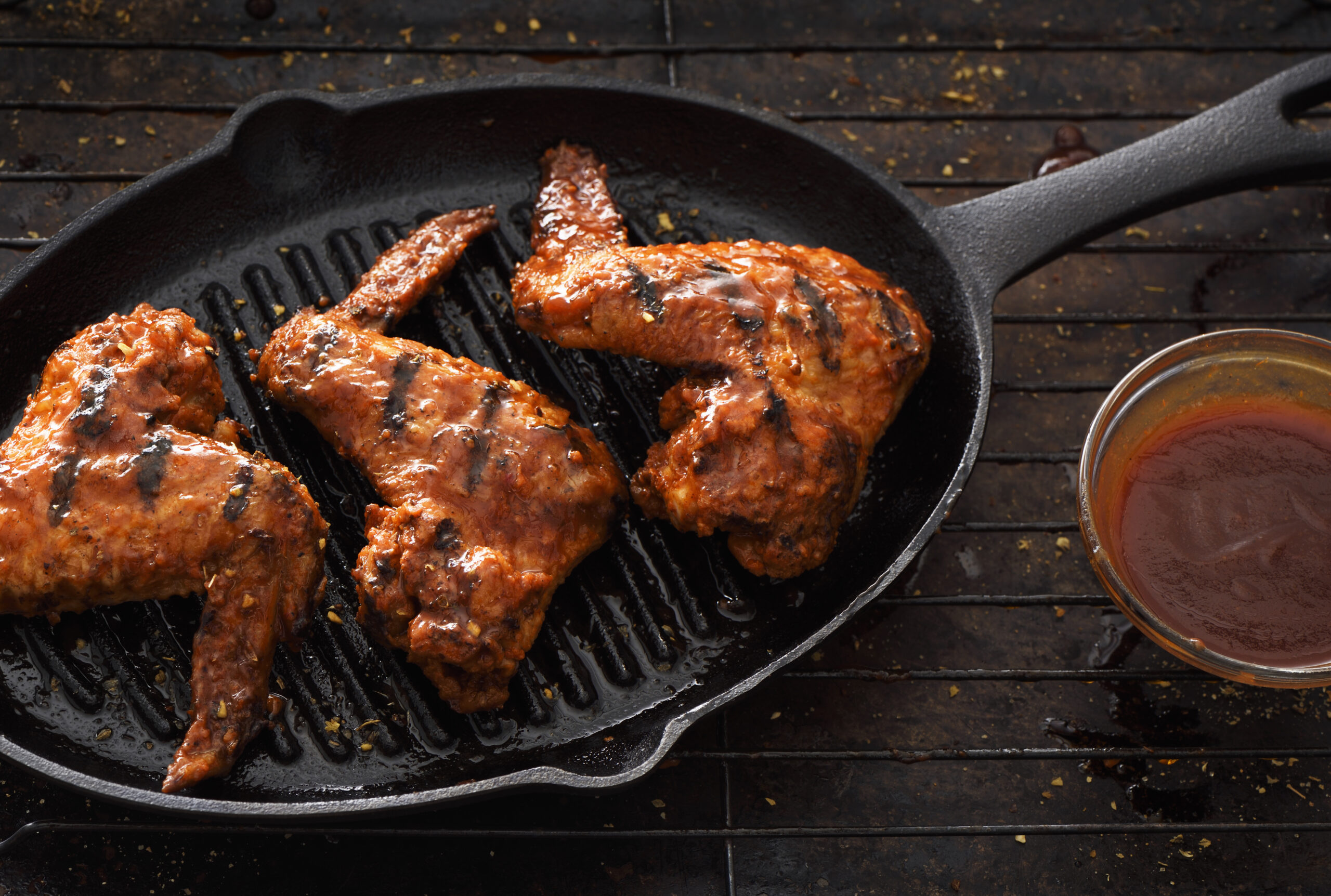 Barbecue grilled chicken wings in a griddle on a dark background