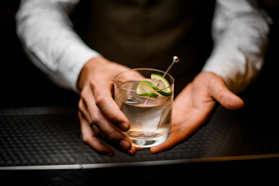 beautiful close-up on hands of man bartender holding glass with cold drink with ice cube decorated with lime