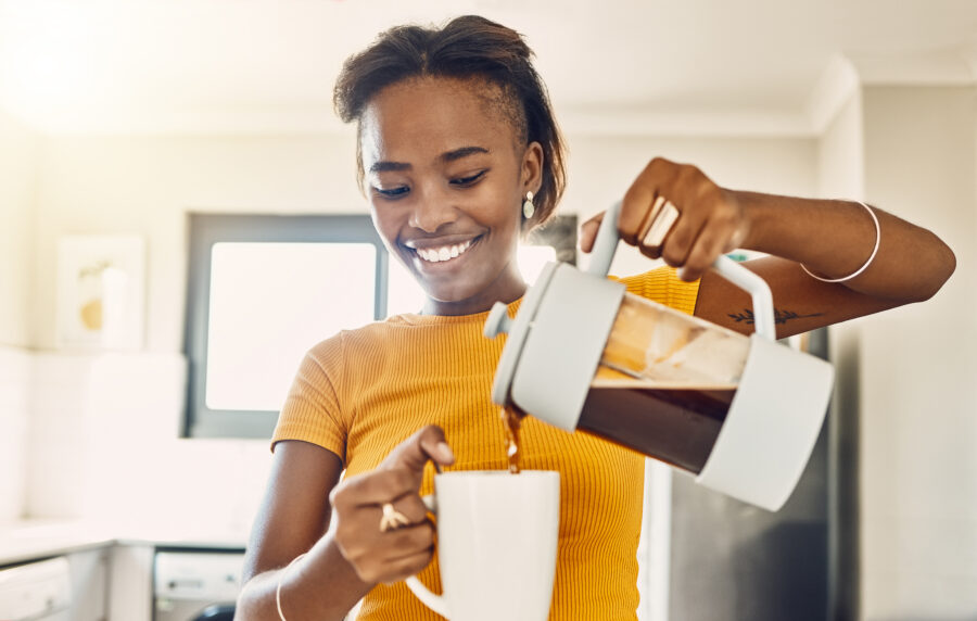 woman making coffee and pouring hot beverage in cup for morning home kitchen routine.