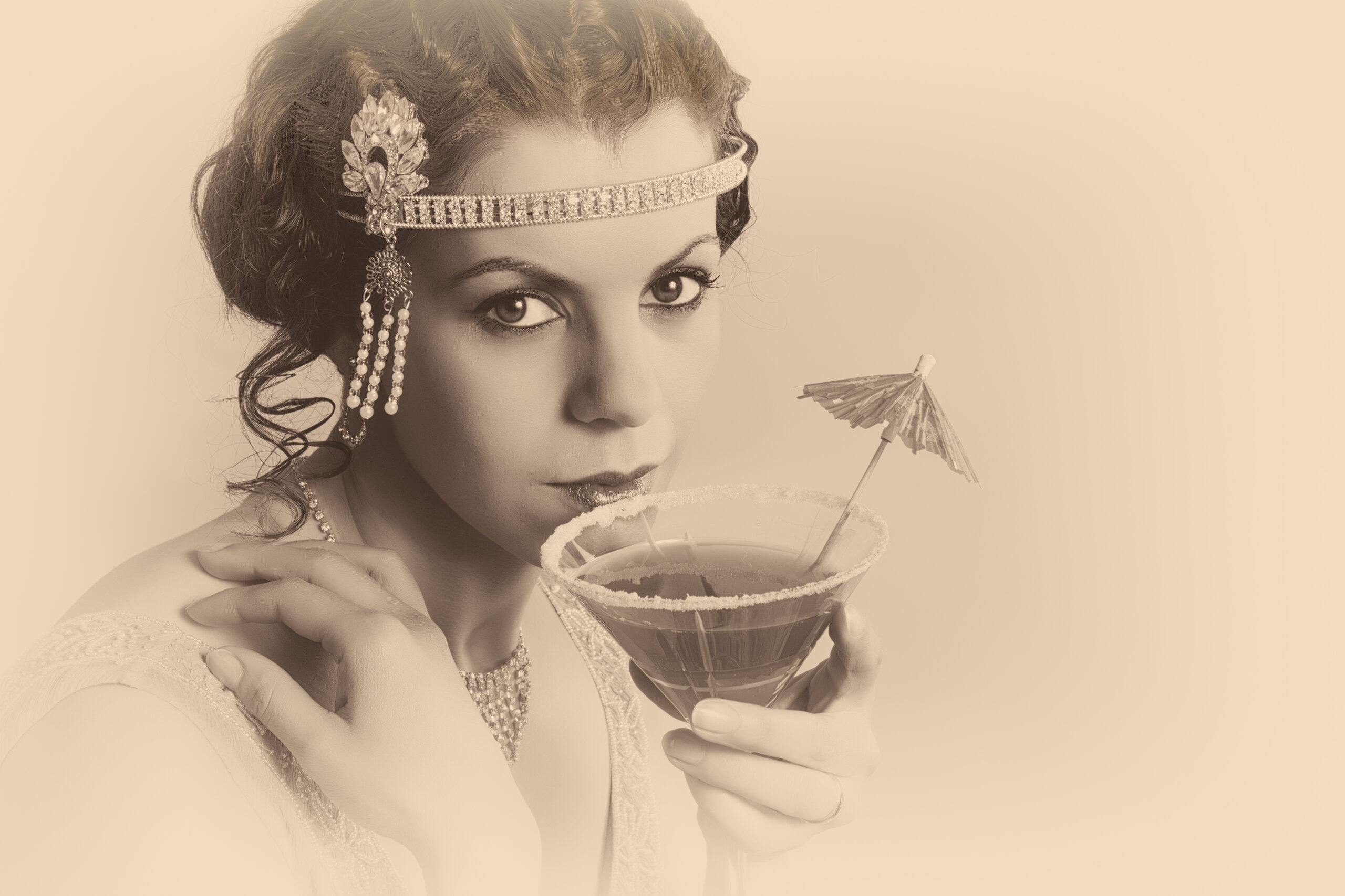 Beautiful young vintage 1920s woman with headband and flapper dress drinking a cocktail