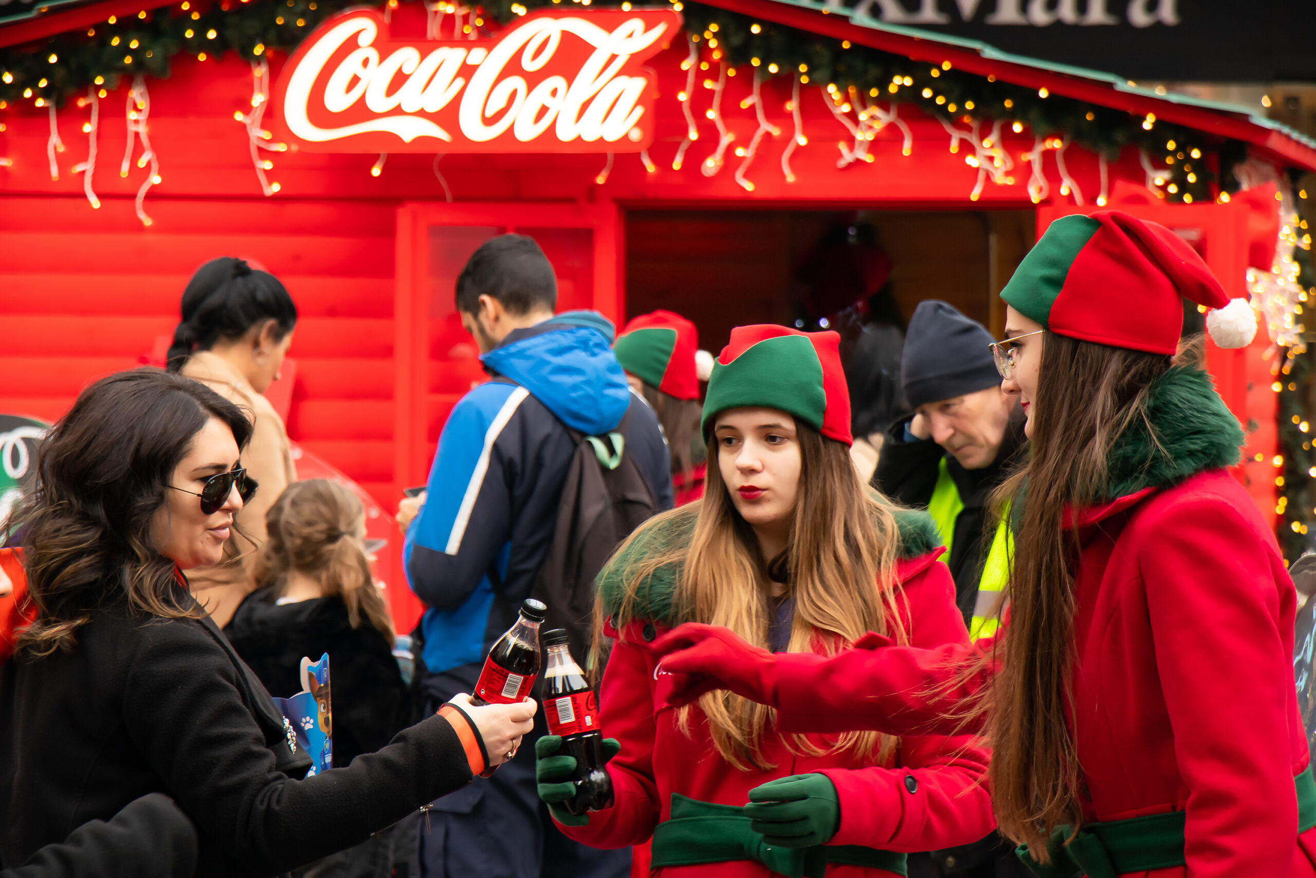 Young Coca Cola promoters giving away free drinks to people during Christmas holiday promotion campaign on city street