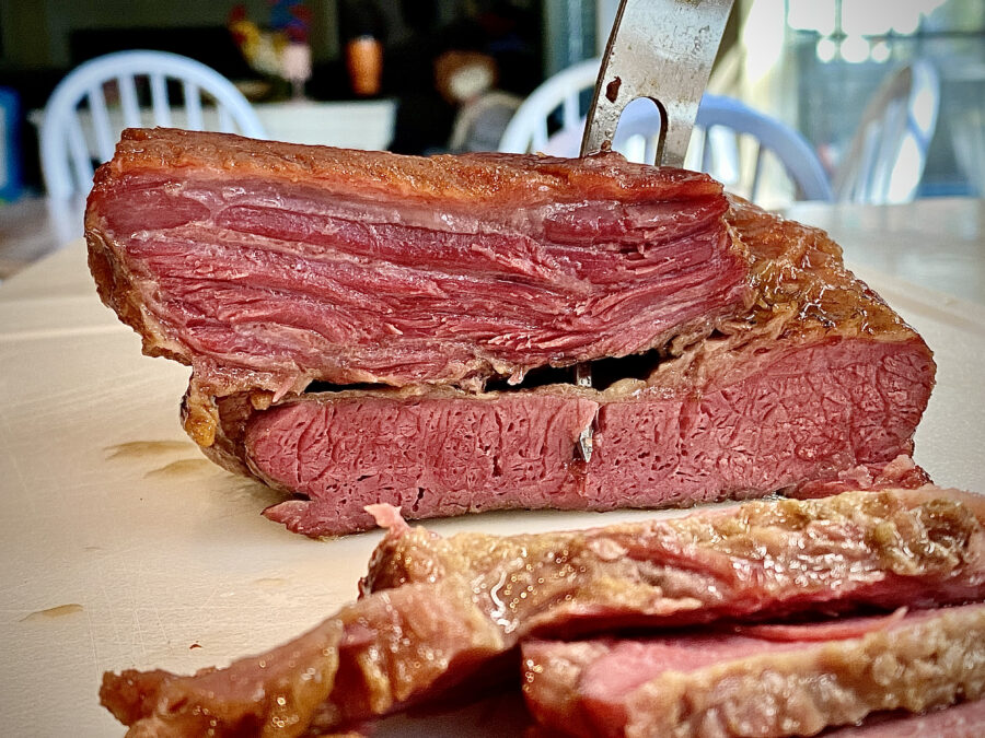 Big flat of corned beef brisket cooked in Guinness beer, being sliced.