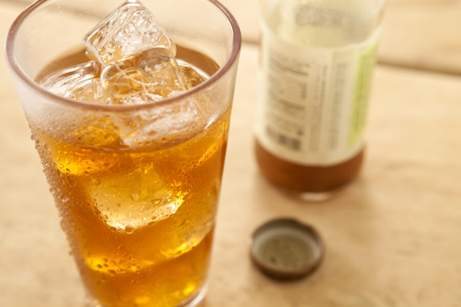 Big glass of iced tea with bottle and cap in background.