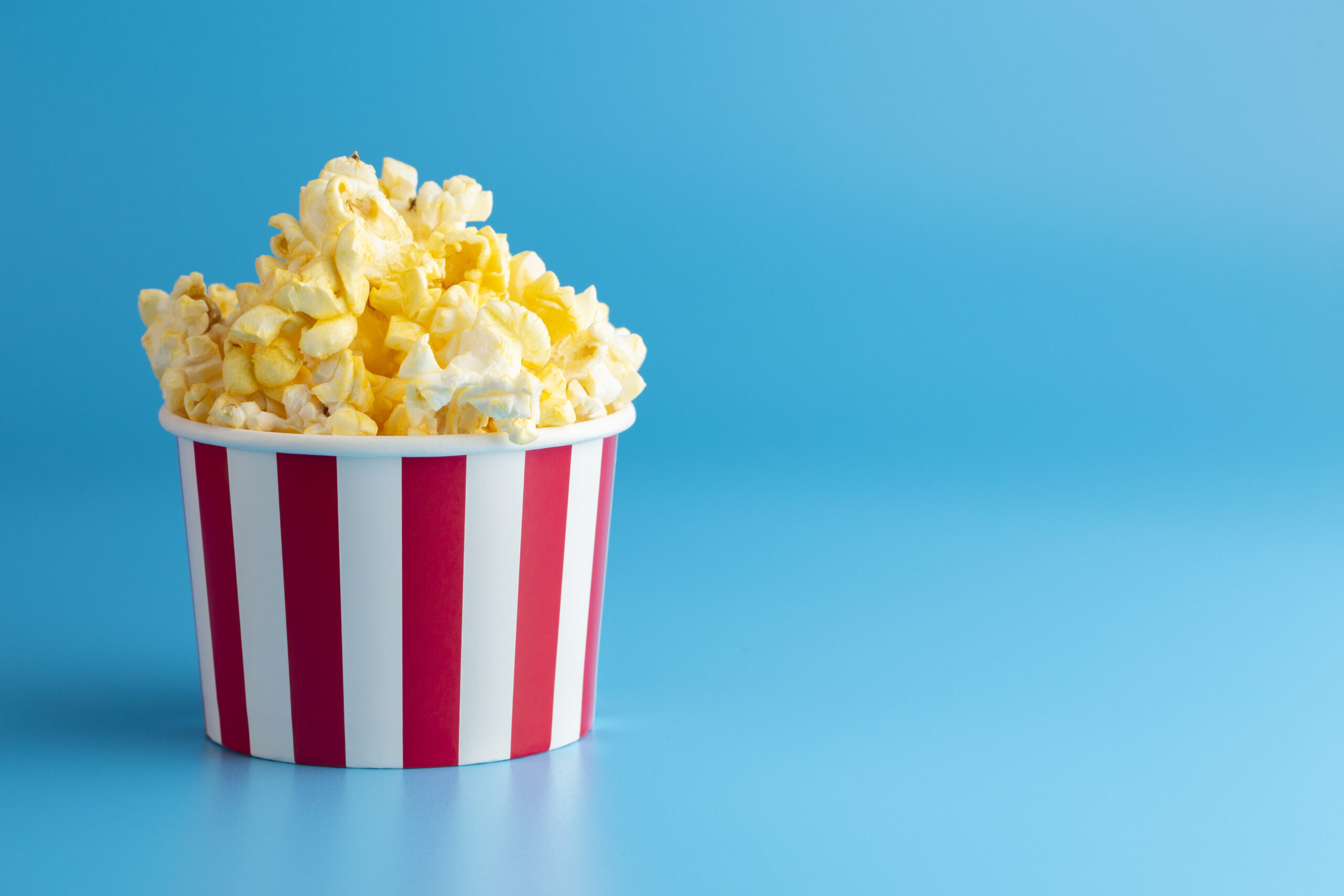 Buttter Popcorn in a Red and White Striped Container on a Blue Background