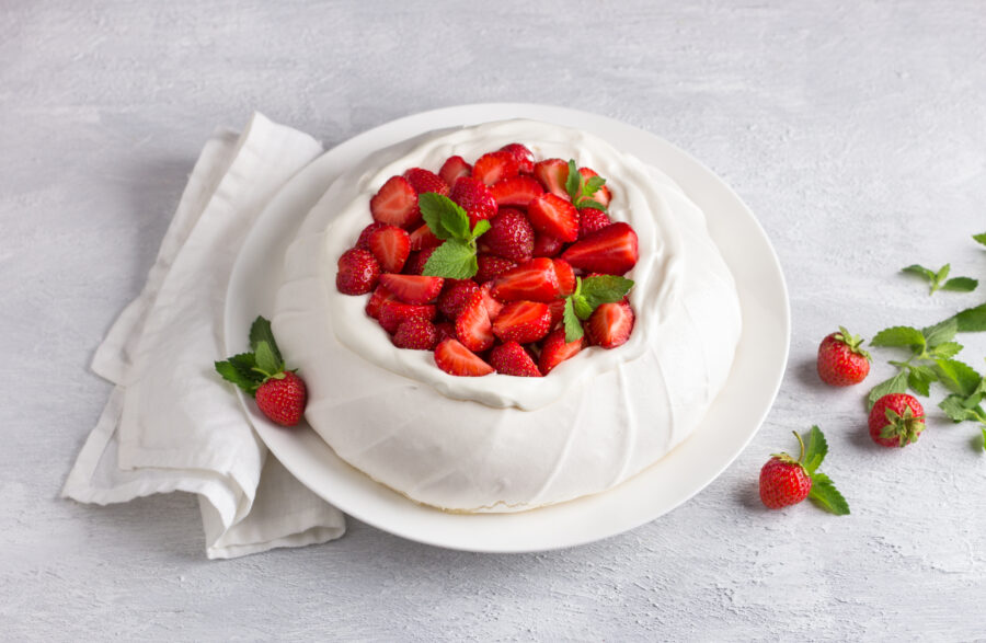 Classic Pavlova meringue cake with whipped cream and strawberries, sprinkled with powdered sugar on light gray textured background, selective focus