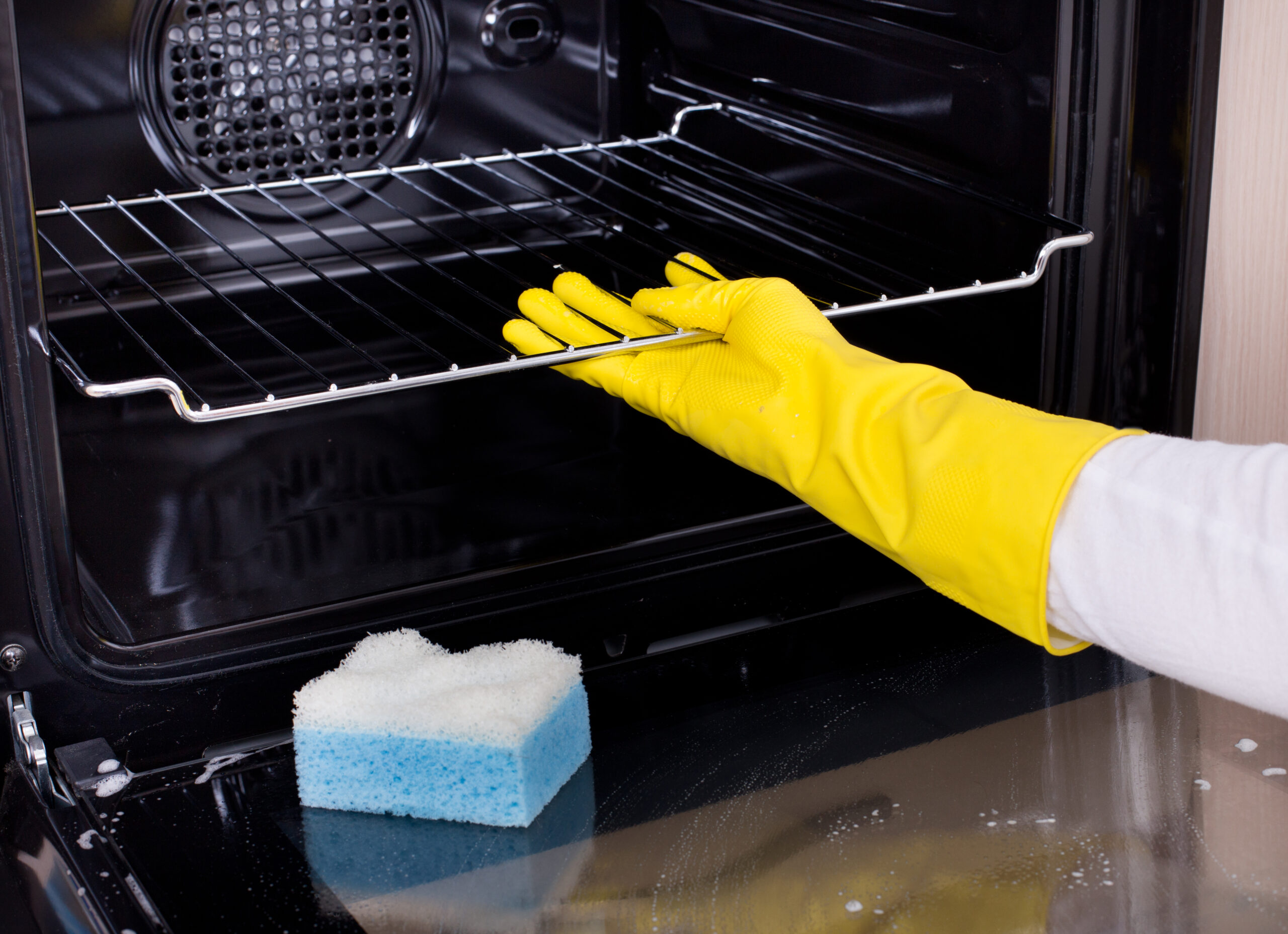 Close up of female hand with yellow protective gloves cleaning oven