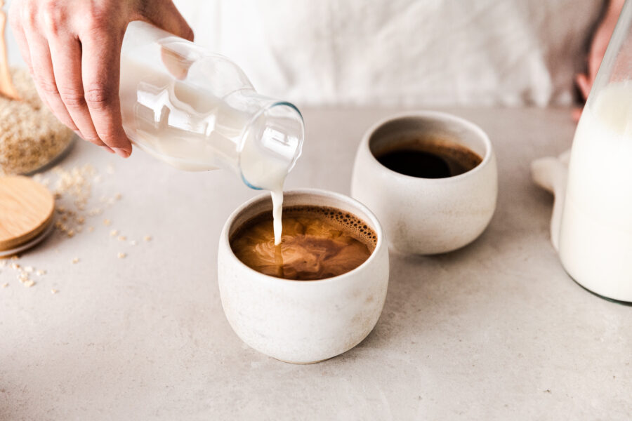 Close-up of pouring oat milk into black coffee cup. 