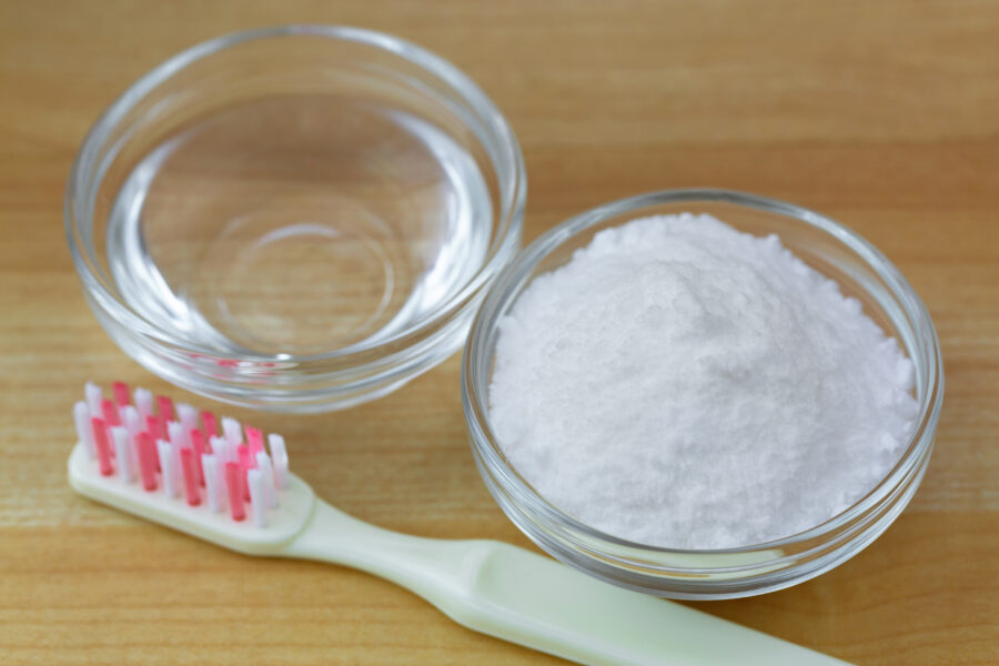 Closeup of baking powder next to vinegar, toothbrush on wooden background. 