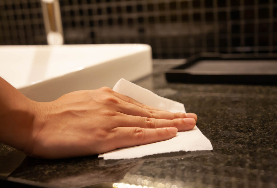 Closeup of hand using paper wipe cleaning dark stone marble surface. Concept of disinfection surface to prevent coronavirus infection, get rid of dust, germs. Selective focus.