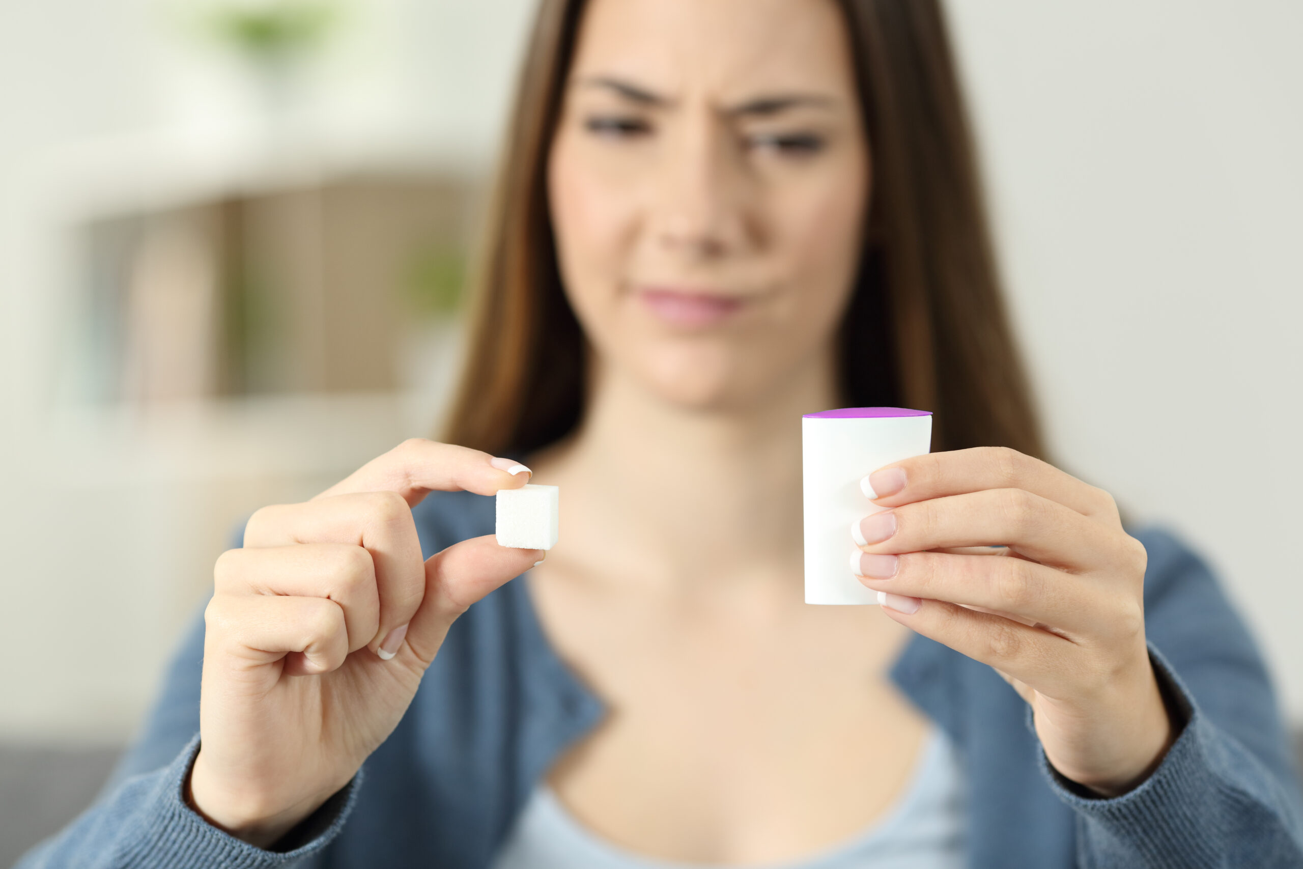 Confused woman doubting between saccharine and sugar at home