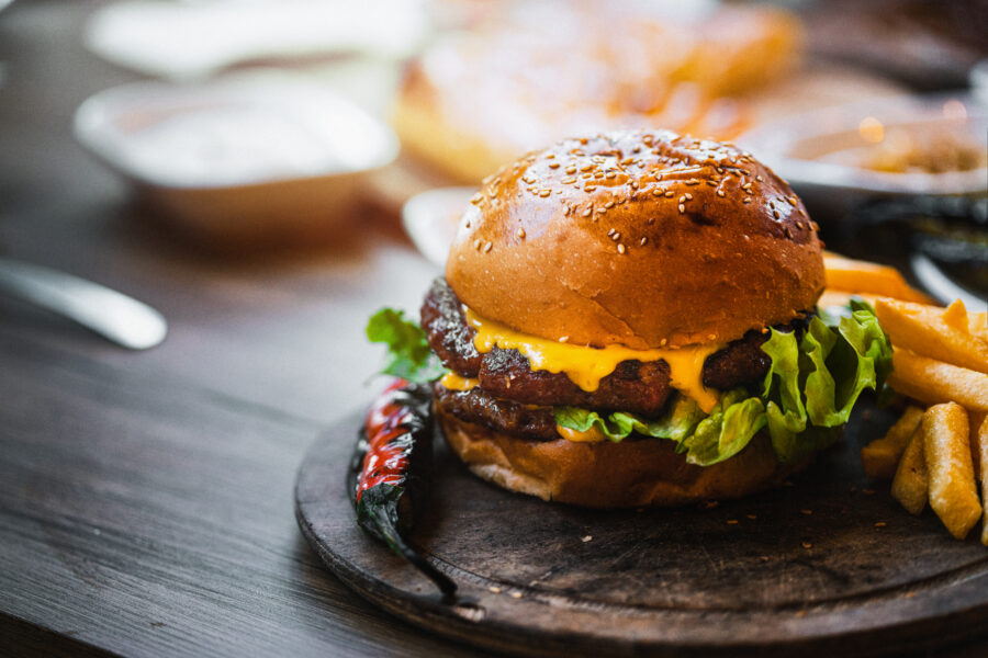 Delicious double burger with french fries and vegetables on wooden cutting board