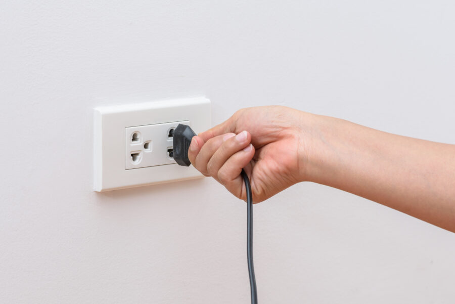 Female hand trying to plugging in appliance to electrical outlet in wall.