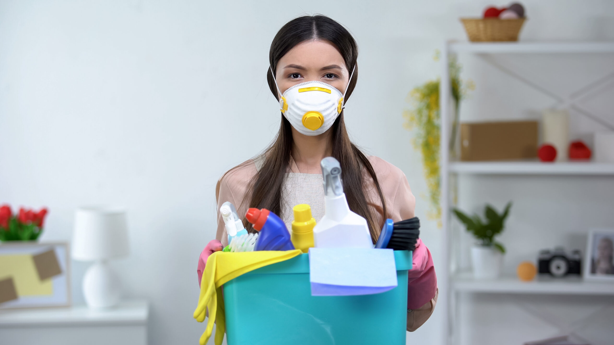 Female in respirator holding basket with household chemicals, health risk