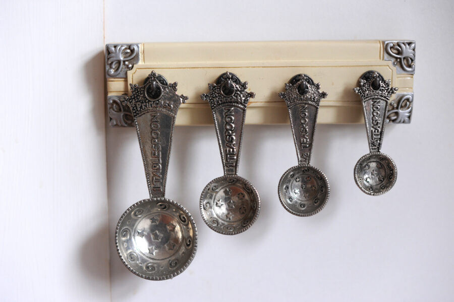 Four measuring spoons arranged from largest to smallest, hanging on a wall.