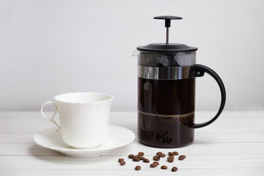 French-pressed ground coffee and a white porcelain cup and saucer. 