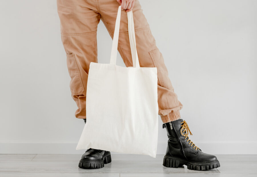 Girl in boots and pants holding cotton linen eco bag mockup. Woman legs with environment friendly shopping handbag with empty copy space for business