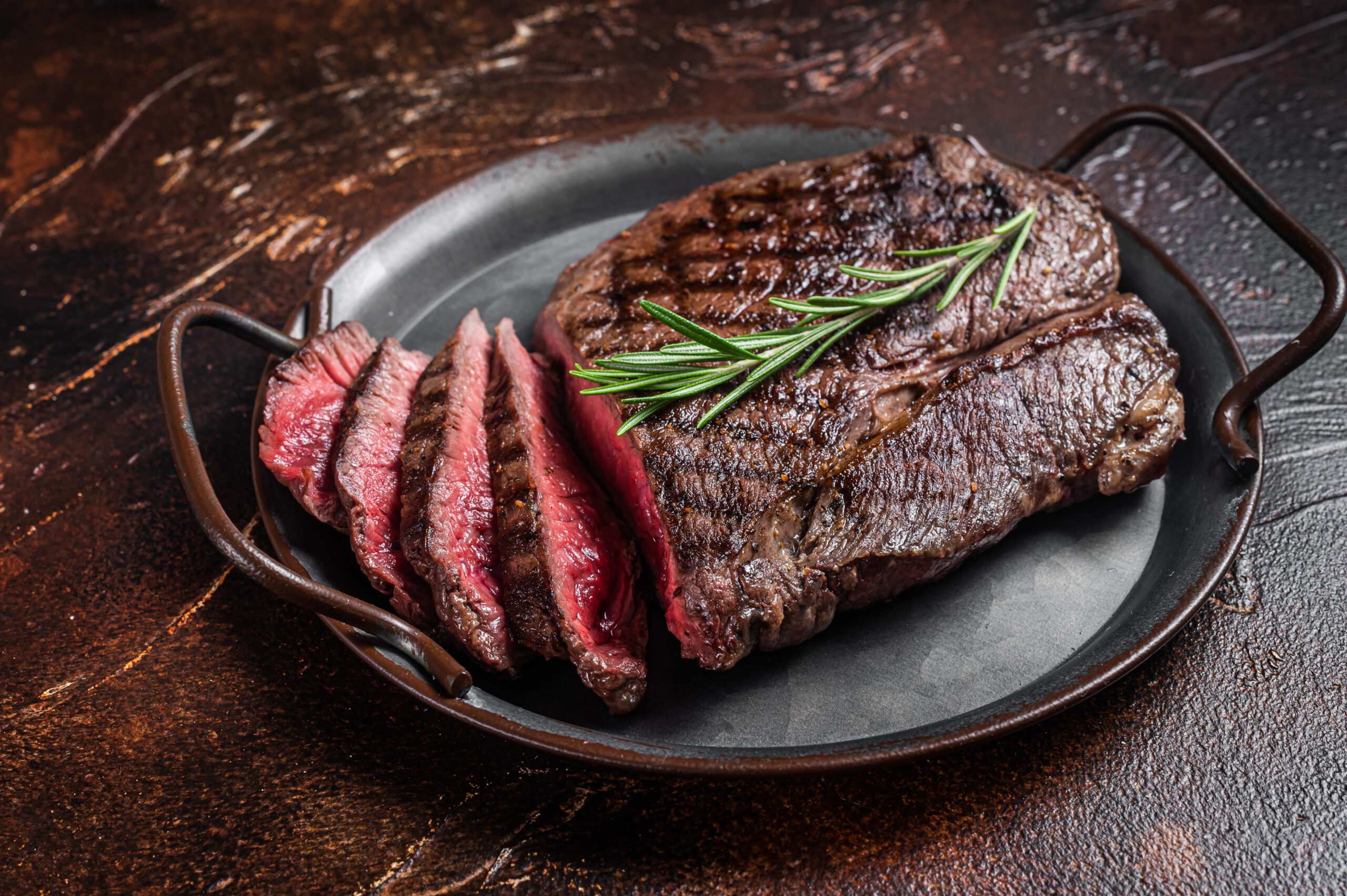 Grilled Medium Rare top sirloin beef steak or rump steak on a steel tray. Dark background. Top view.